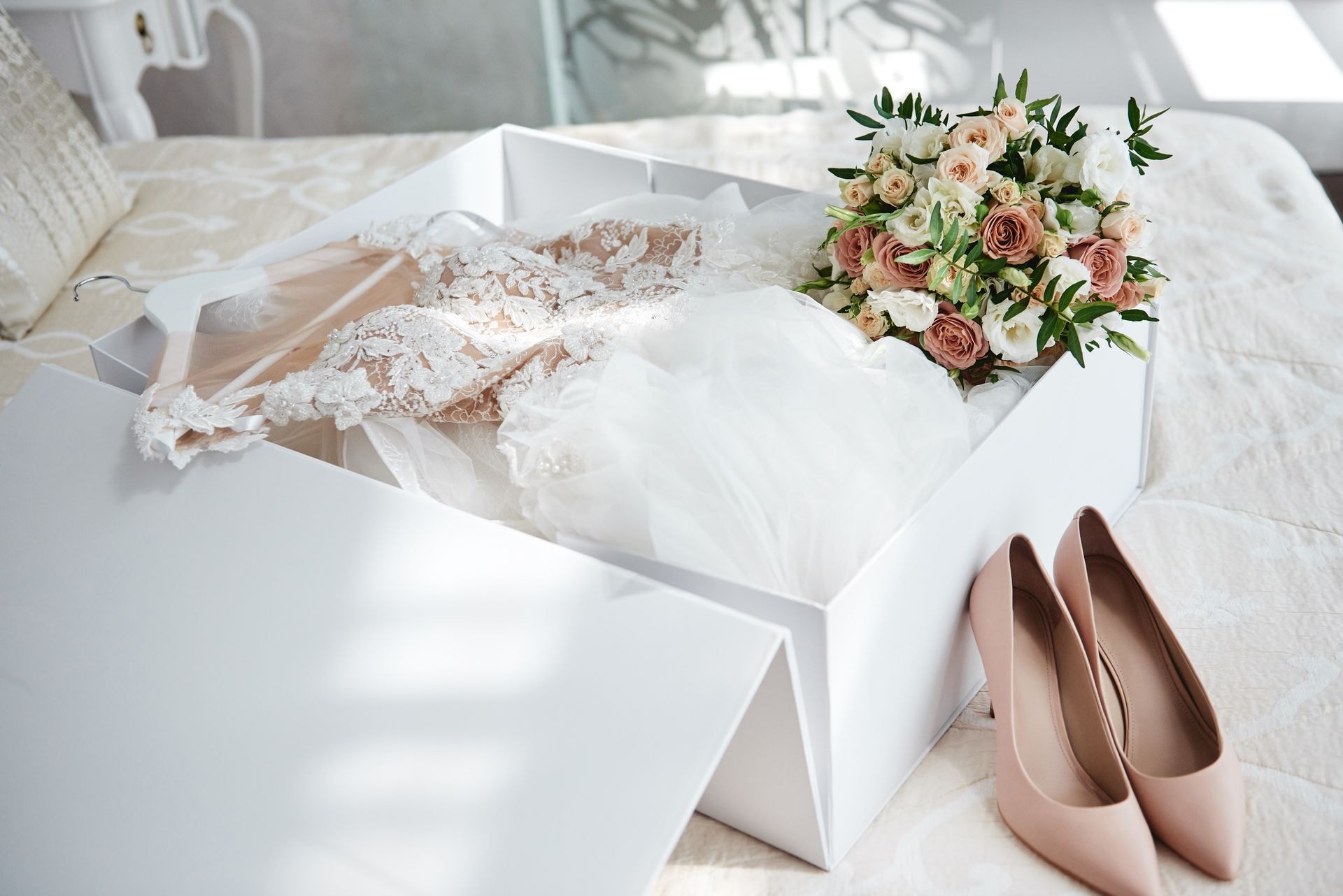 Wedding gown arranged in white box with bridal bouquet and elegant shoes